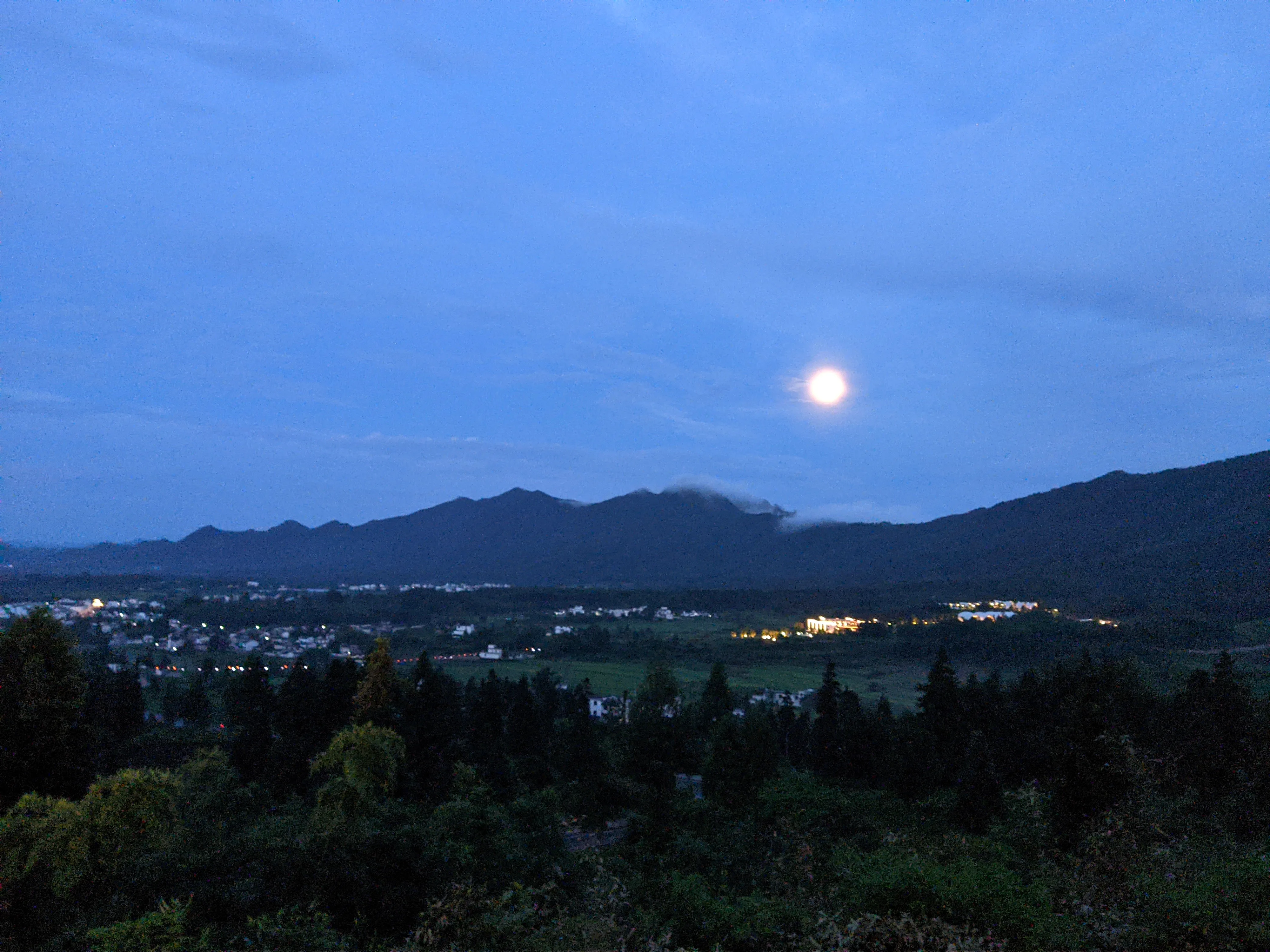 圆月升过层叠山影，村镇灯火在蓝调时刻亮起。